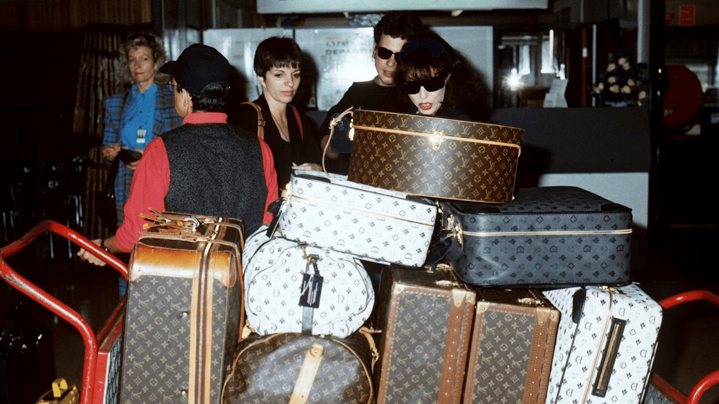 A pack of luggage accompanied by some travelers