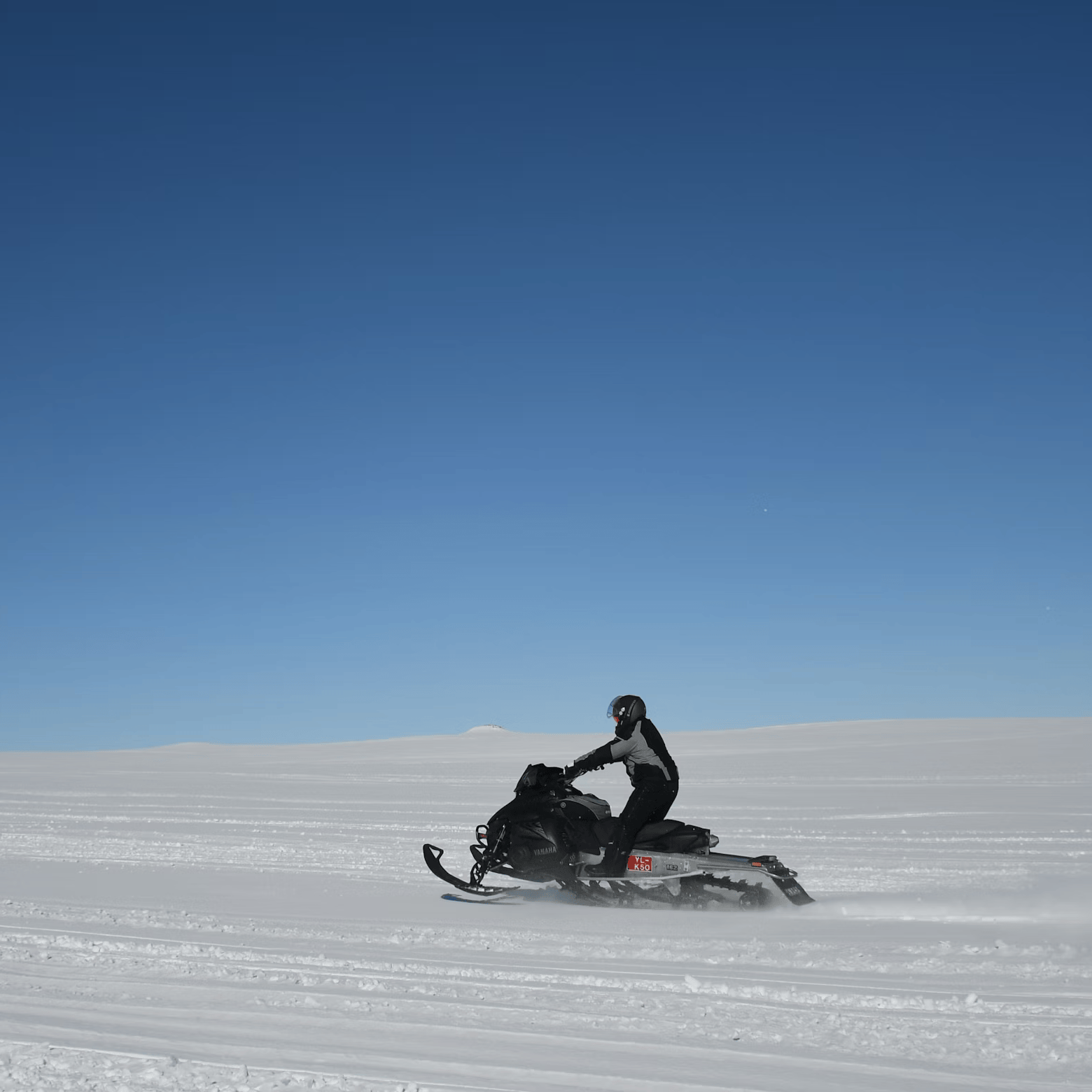 Person on a snowmobile in a snowy landscape with clear blue sky